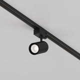 The Vuoro S 3-Circuit Trinity Track LED Spotlight, 10W 4000K in black, features a cylindrical design with an adjustable swivel head and is mounted on a 3-circuit track rail, casting downward light against a white ceiling.