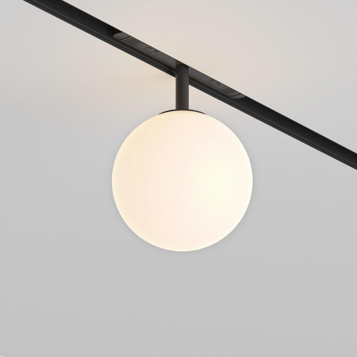 A spherical Luna LED Magnetic Exility Track Globe Ceiling Light, 5W 3000K, elegantly attached to a black track, emits a soft glow against a plain white ceiling.