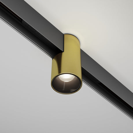 The Alfa CCT LED Dimmable Magnetic Exility Track Downlight 7W 2700-6000K - Brass casts a soft glow downward from its sleek cylindrical gold casing with an elegant brass finish, attached to a black track on a white ceiling.