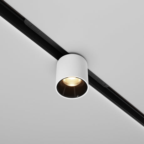 The Alfa S LED Magnetic Exility Track Downlight 7W 3000K in white is mounted on a black track on a white ceiling, emitting warm light. Its simple and modern design enhances ambiance while offering energy efficiency.