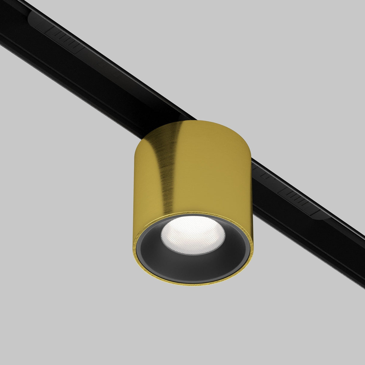 An Alfa S CCT LED Dimmable Magnetic Exility Track Downlight in brass, attached to a black track on a gray background, is illuminated, casting a bright circular glow.