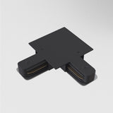 The Unity Tracks Recessed L-Shaped Connector in black, featuring visible screws and two short extensions, is mounted on a smooth white surface in contemporary spaces and appears to be part of structural or electrical assemblies.