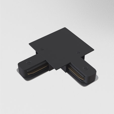 The Unity Tracks Recessed L-Shaped Connector in black, featuring visible screws and two short extensions, is mounted on a smooth white surface in contemporary spaces and appears to be part of structural or electrical assemblies.
