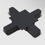 A modern abstract sculpture, the Unity Tracks Recessed X-Shaped Connector in black metal, is mounted on a white wall. It features a central square with extending arms like an X, showcasing rounded edges and visible screws.