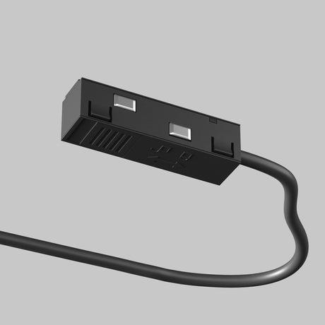 Close-up of the Exility Track Power Feed - Black (TRA034B-42B-1), featuring a sleek design with two three-prong outlets, ideal for modern interiors. A spiral black cord extends from the strip against a plain light gray background, highlighting its elegance for track lighting systems.