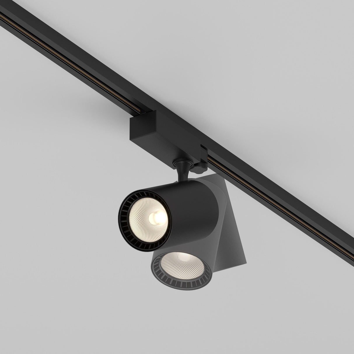 Close-up of a modern Vuoro S 3-Circuit Trinity Track LED Spotlight on the ceiling, featuring two adjustable LED spotlights. One is lit, casting a soft glow, while the other is off. This IP20-rated 20W black fixture boasts minimalist and contemporary design with a 3000K warmth.