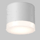 The Pauline Round Surface Downlight - White is a sleek cylindrical ceiling fixture with water droplet details hinting at suitability for damp areas. It emits a soft glow, enhancing its minimalist charm against a plain light gray backdrop.