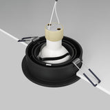 Close-up of the Atom Single Tilt Round Recessed Downlight - Black, partially installed in a white ceiling. It features an adjustable tilt cylindrical socket with extending wires, surrounded by circular black housing and spring clips for secure mounting.