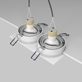 The ceiling view features two Atom Twin Tilt Recessed Downlights in white, with spiral cords and metal springs, against a gray and white backdrop. Their adjustable tilt ensures ideal ambient lighting for any room.