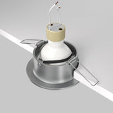 An image shows a Slim Fixed Round Recessed Downlight - Silver being installed in a neutral ceiling. The fixture has cast aluminum housing and two metal clips on the sides, with electrical wires extending from the center.