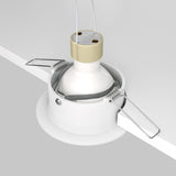 The Slim Fixed Round Recessed Downlight in white features a gold and white cylindrical design with spring-loaded clips for easy installation, offering a minimalist lighting solution partially set in a white ceiling for an elegant room accent.