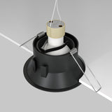 Close-up of the Dot Single Tilt Round Recessed Downlight in black, showcasing its adjustable tilt mechanism and white connector with metal spring clips against a gray background, angled to highlight its installation method.
