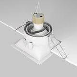 A Dot Single Tilt Square Recessed Downlight - White is being installed, featuring a tilt mechanism, LED lighting, springs, and a square housing. Its mounted into a square ceiling opening with visible wires.