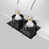 Two Dot Twin Tilt Recessed Downlights in black are shown partially installed in a white surface. These energy-efficient LED fixtures feature white bulbs, visible spring clips, and wires extending from the top.