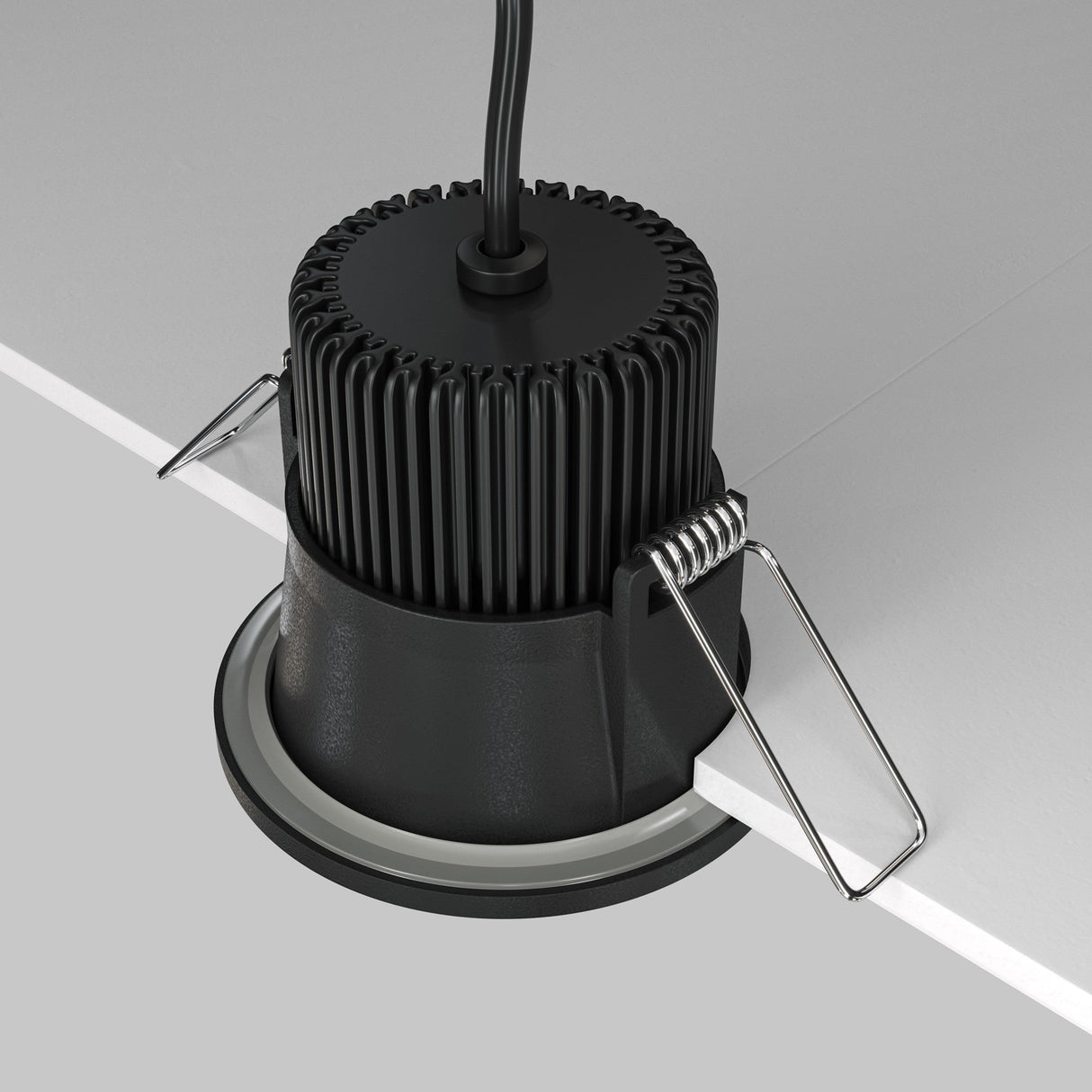 A Zoom LED Round Recessed Downlight 6W 3000K is installed into a ceiling, featuring a black, ridged heat sink and metal spring clips on each side secured to a white panel. With an IP65 rating for protection and a black power cable for optimal performance.