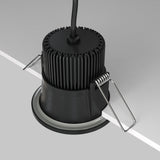 A Zoom LED Round Recessed Downlight 6W 3000K is installed into a ceiling, featuring a black, ridged heat sink and metal spring clips on each side secured to a white panel. With an IP65 rating for protection and a black power cable for optimal performance.