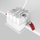 A white geometric Alfa LED Fixed Square Recessed Downlight emits a cool 4000K light. A white wire extends from the top, with a red-handled tool featuring twin metal prongs on its side, reminiscent of modern interior lighting.