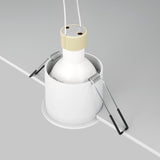 Close-up of the Reif Round Recessed Downlight - White, featuring a cylindrical design ideal for modern spaces. The image displays installation parts such as spring clips and wires, spotlighting the fixture partly embedded in a surface, crafted from premium materials.