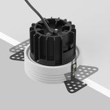 Close-up of a white Round LED Recessed Trimless Downlight 12W 3000K with a circular base and mounting brackets. Showcasing minimalist design, a black cable extends from the top against a gray background, offering energy-efficient style.