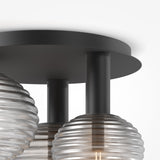 Close-up of the Reels 3 Light Semi-Flush - Black, showcasing its industrial design with three translucent ribbed glass globes on cylindrical black metal stems connected to a circular black base, reflecting the essence of a sleek black ceiling light.