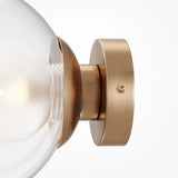 A close-up of the Basic form Big Clear Ball Wall Light - Gold, featuring an opal glass globe and a sleek, brushed brass base. The softly illuminated bulb enhances the refined elegance of this luxury lighting design.