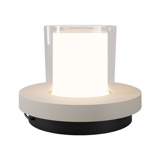 Maytoni Lantra rechargeable LED table lamp with frosted acrylic diffuser in a clear cylinder on a white and black round base, shown lit.