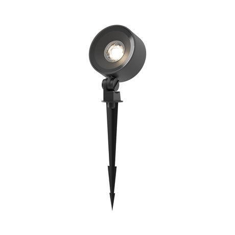 Maytoni Core 25W LED bollard light in black aluminium with a round tilting spotlight head on a ground spike, illuminated on a white background.
