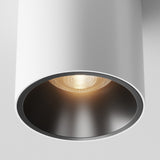 Close-up of the Alfa LED Round Surface Downlight 12W 3000K in white and black. The warm white LED light casts a cozy glow from its black-lined cylinder, perfect for modern interiors, with the textured bulb subtly visible against the plain white ceiling.