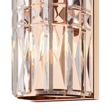 Close-up of a Facet 3 Light Long Wall Light - Gold, featuring geometric crystal faces that create a reflective, prismatic effect. The interior light casts a warm glow, highlighting the amber and copper tones of its gold metal finish frame.