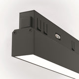 A modern black Basis DALI CCT 12W LED Linear Track Light with dimmable smart lighting (2700-6000K), showcasing a sleek, smooth surface with visible screws. It emits a bright white glow from the underside and is mounted against a light-colored wall.