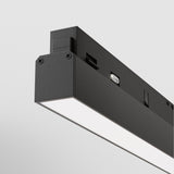 A close-up view showcases the minimalist design of the Basis CCT LED Dimmable Linear Track Light in black on a white ceiling. This sleek fixture features a smooth illuminated panel, customizable with 24W, 2700-6000K, and controlled seamlessly via Bluetooth Mesh.