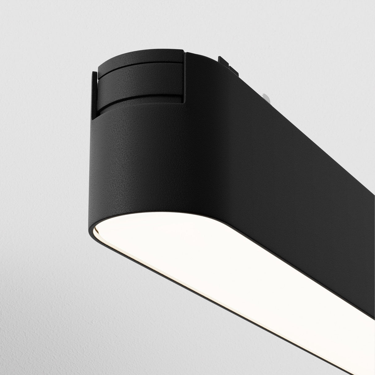 The Basis LED Linear Track Light for Magnetic Tracks Radity 6W 4000K, a modern rectangular black fixture with rounded edges, hangs against a white ceiling, offering neutral illumination as part of contemporary lighting solutions.