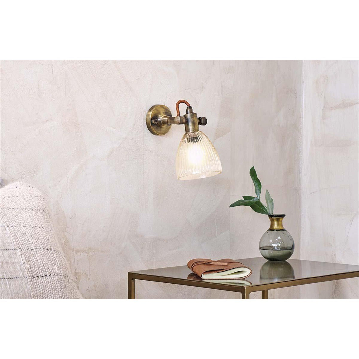 Rarni Recycled Glass Wall Light in antique brass with ribbed glass shade and rust fabric flex, shown mounted beside a side table in a living room setting.