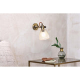 Rarni Recycled Glass Wall Light in antique brass with ribbed glass shade and rust fabric flex, shown mounted beside a side table in a living room setting.