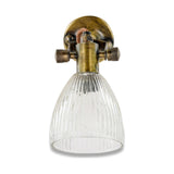 Rarni single wall light in antique brass with a round back plate, knurled thumbscrews, and a ribbed recycled glass tulip shade, shown on a plain white background.