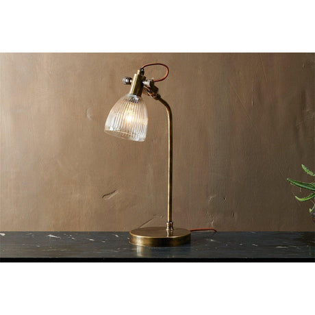 Rarni Recycled Glass Table Lamp in antique brass, with ribbed glass dome shade on curved stem and round base, shown lit on a dark marble surface.