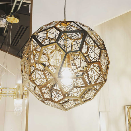 The Rango Acid Large Pendant Light – Brass features a geometric spherical design with intricate polygonal patterns, hanging from the ceiling and illuminating the room with a bright central bulb.