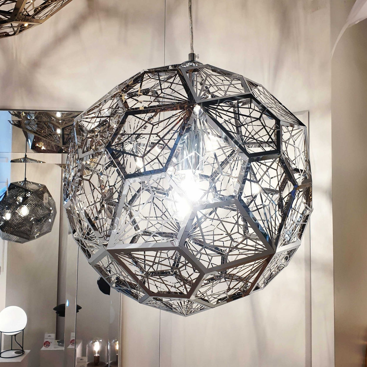The Rango Acid Large Pendant Light in silver features a geometric, spherical design with intersecting lines, bringing modern sophistication to any room with its striking presence and reflective elegance.