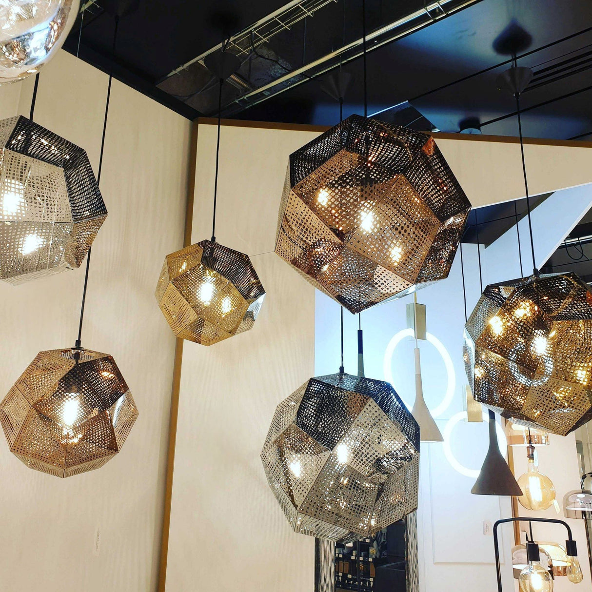 The Rango Small Pendant Light in gold hangs from the ceiling, its geometric faceted shade casting ambient light that enhances a modern interior with neutral walls and minimal decor.