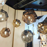 The Rango Small Pendant Light in gold hangs from the ceiling, its geometric faceted shade casting ambient light that enhances a modern interior with neutral walls and minimal decor.
