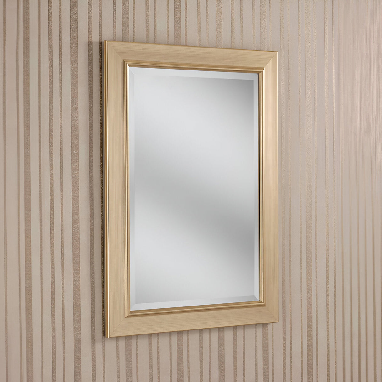 The Rimini Rectangle Wall Mirror - Gold, featuring its luxurious light wooden frame, is mounted on a wall decorated with vertical beige and light brown striped wallpaper. The mirror gracefully reflects a soft, neutral interior that exudes understated elegance.