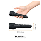 A person's hand gripping the black Duracell Rubber LED Flashlight, highlighting its compact dimensions. This 80-lumen flashlight measures 6.1 inches in length and 1.7 inches in diameter, with the Duracell logo prominently displayed beneath its surface, offering dependable performance whatever the circumstances.