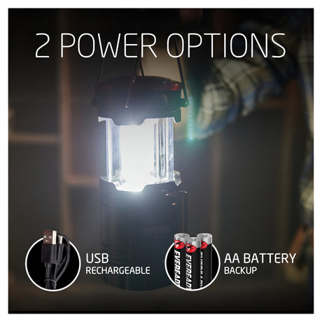 The Eveready 2 in 1 Hybrid Powered Lantern 300 Lumen features "2 Power Options" prominently displayed above it. The left inset highlights a USB cable for USB and battery charging, while the right displays three AA batteries for backup. A blurred background adds to the ambient mystery with a hint of a person's arm in the scene.