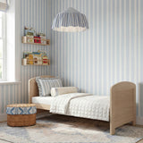 Seeker Convertible Cot Bed in Nordic, natural oak-effect toddler bed with rounded headboard and footboard, shown in a nursery with striped blue wallpaper and bedding.
