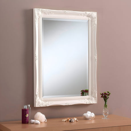 The Mirame Rectangle Wall Mirror in white hangs on a beige wall above a wooden dresser. The dresser is adorned with a small vase of red flowers, a red bottle, a candle, cotton balls, and seashells. This arrangement perfectly complements modern interiors with its elegant simplicity.