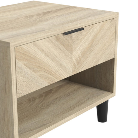 Close-up of the Stockholm 1 drawer bedside table in Sonoma oak effect wood, showing the black bar handle, open shelf, and tapered black leg.