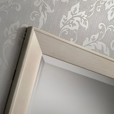 Close-up of the corner of a Sicily Rectangle Wall Mirror - Silver, featuring a wooden frame against textured wallpaper with a floral pattern. The light-colored wallpaper beautifully complements the soft silver hue of this piece, making it ideal for modern home decor.