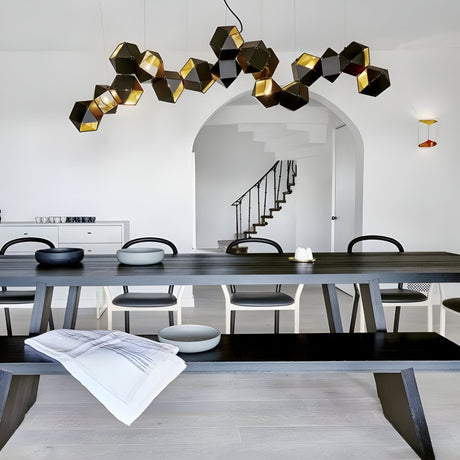 Modern dining room with a long dark wooden table, black chairs, and the striking Spar Linear Suspension Light in Black & Gold. Features white walls, an arched doorway, a staircase with black railing, and minimalist bowls on the table.