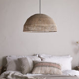 Tivi Natural Jute Lampshade, a wide dome pendant shade in woven jute cord with horizontal bands, hung above a bed with linen pillows in a neutral bedroom.