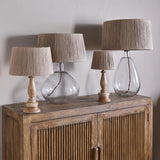 Four table lamps with tapered jute lampshades, including the Tiwa Extra Large in natural, on wooden bases atop a carved wood sideboard against a grey wall.